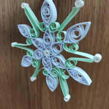 A snowflake ornament made out of paper coils through paper quilling.