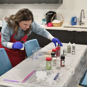A woman in an apron and rubber gloves picking out a color of glitter to use